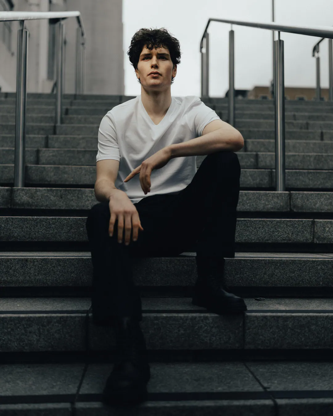 Man in a white T-shirt and black trousers sitting on wide granite steps between metal handrails