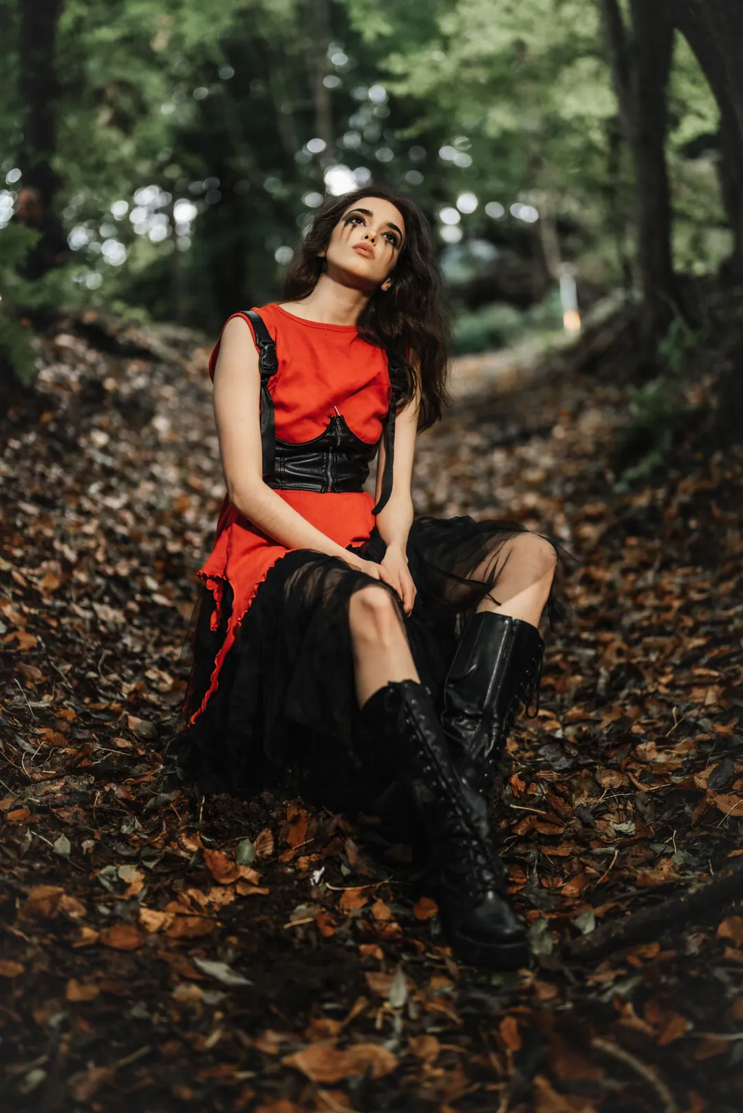 Woman in a red dress, black corset belt and lace skirt sitting on fallen leaves in woodland
