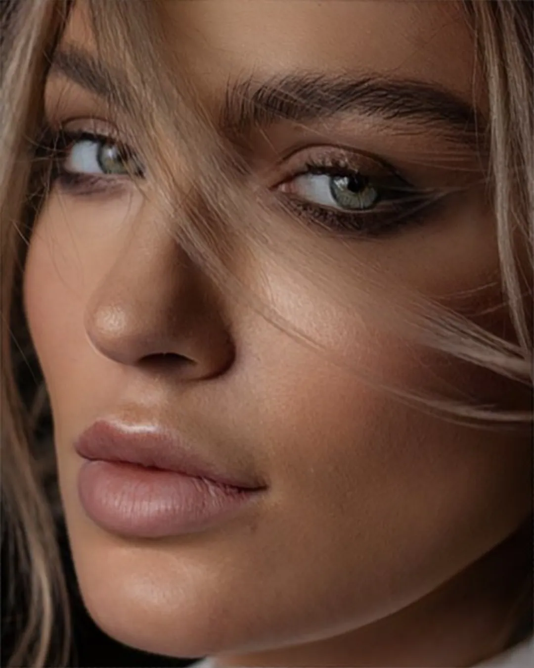 Woman's face in extreme close-up, strands of hair blowing across her eyes in warm soft light