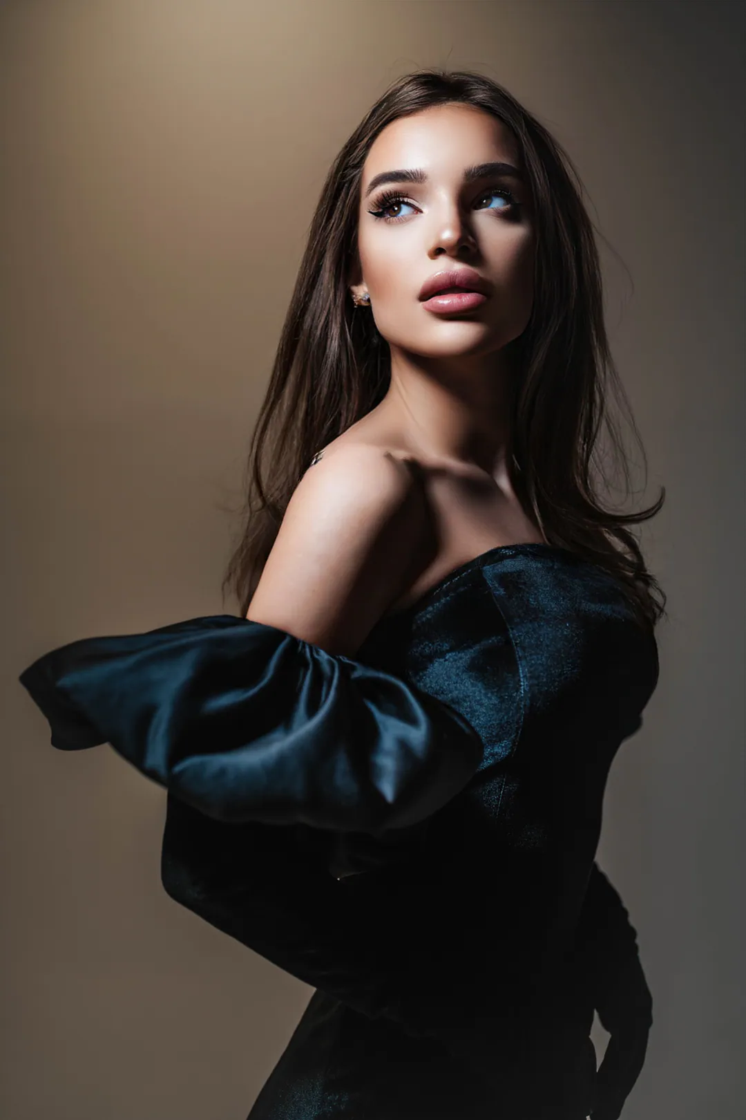 Woman in a black satin dress with voluminous sleeves looking over her shoulder against a warm beige backdrop
