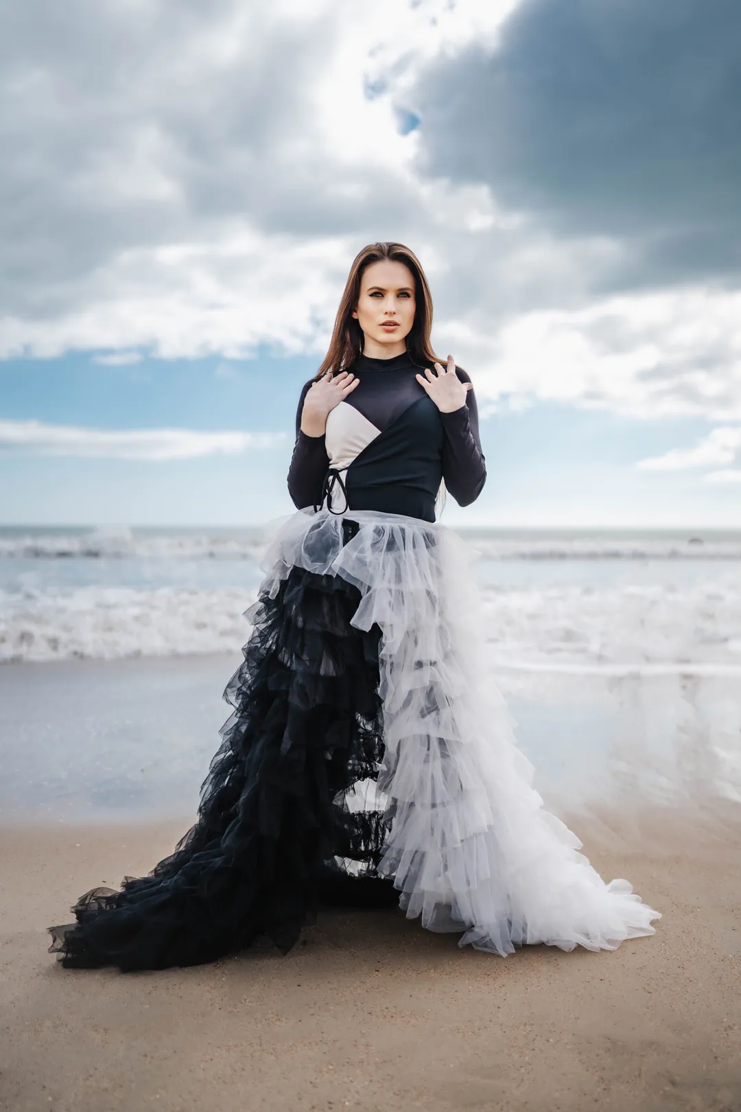 Woman in a black long-sleeved bodysuit and tiered black and white tulle skirt standing on a sandy beach