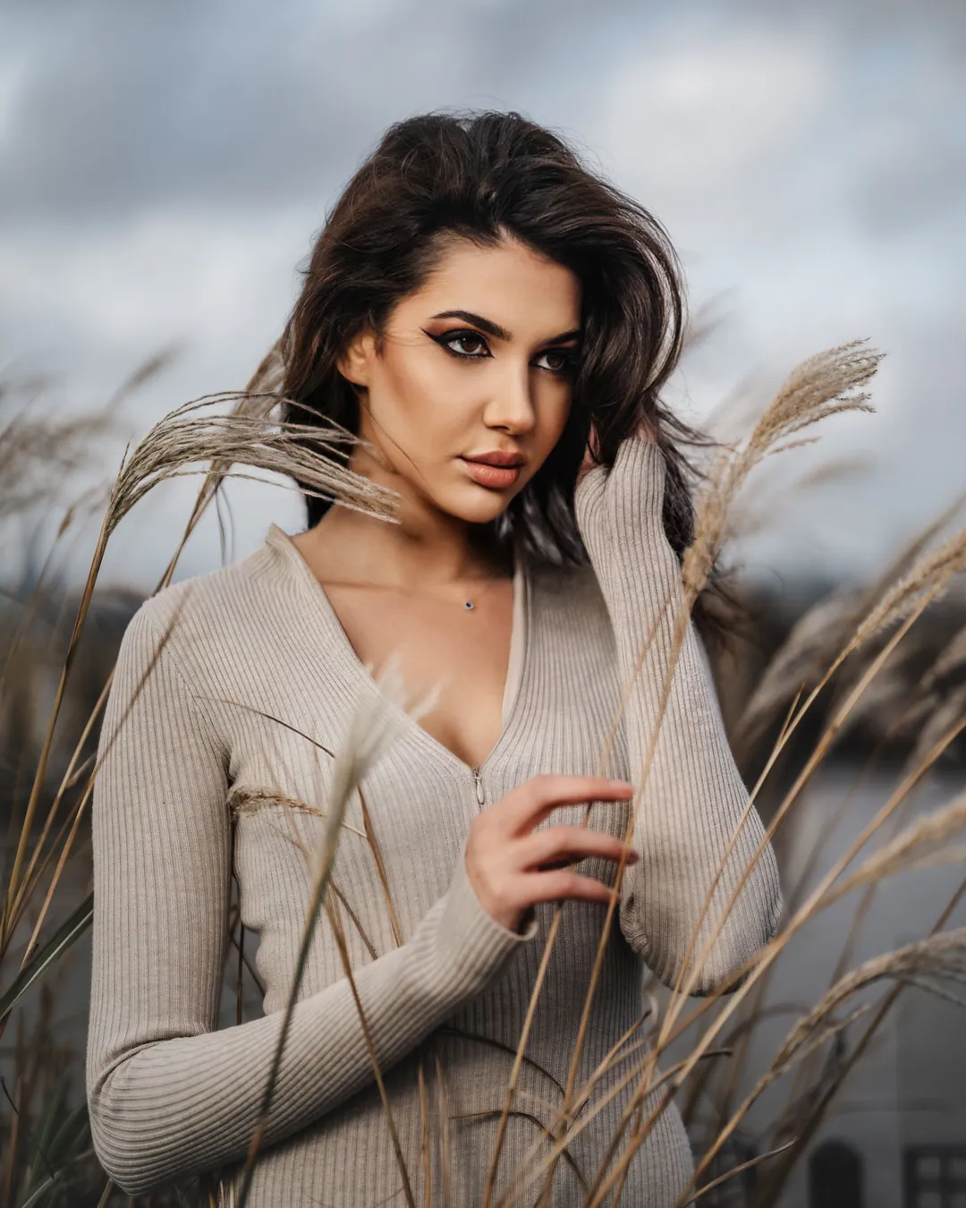 Woman in a ribbed beige cardigan standing among tall pampas grasses under a cloudy sky