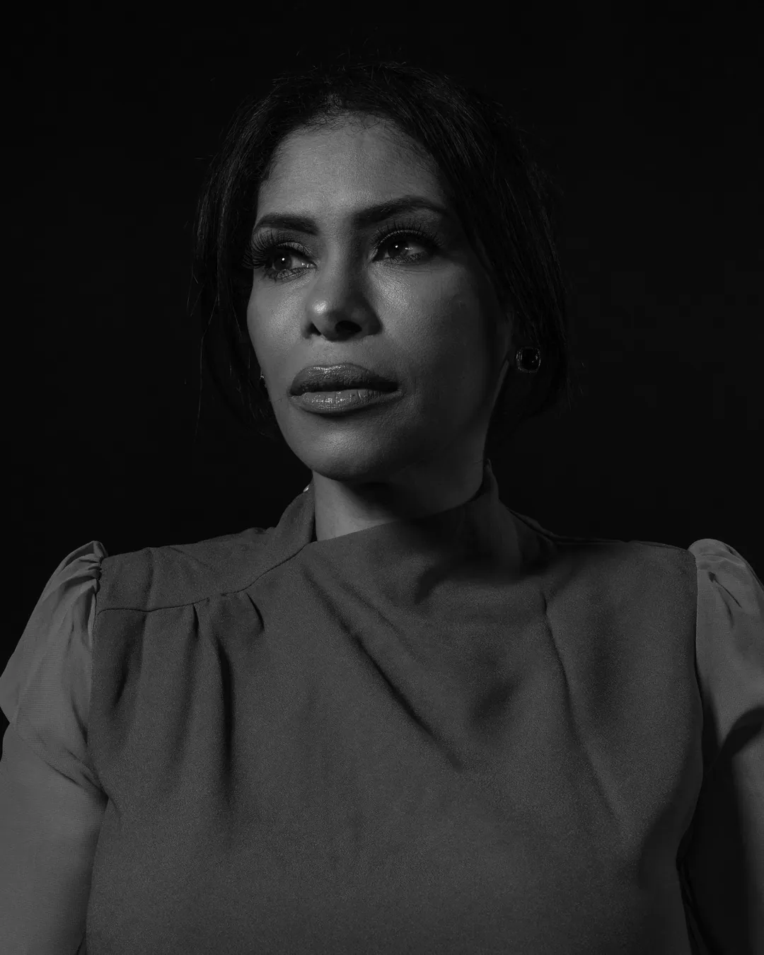 Woman with dark hair in a puff-sleeved top gazing off camera, black and white low-key portrait