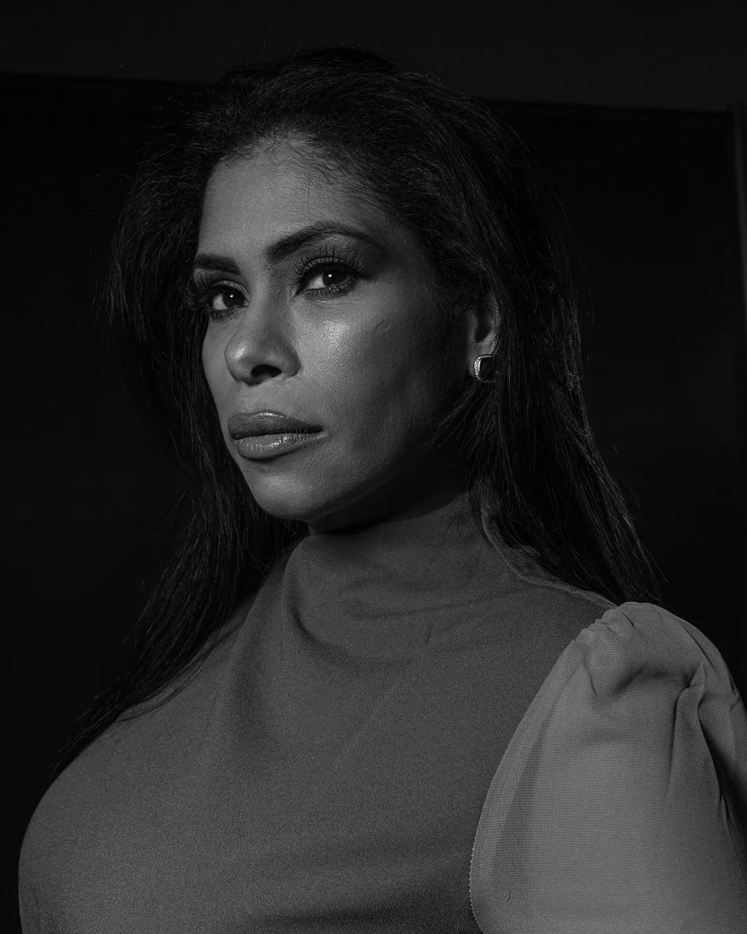 Woman with long hair in a high-neck top looking over her shoulder at the camera, black and white