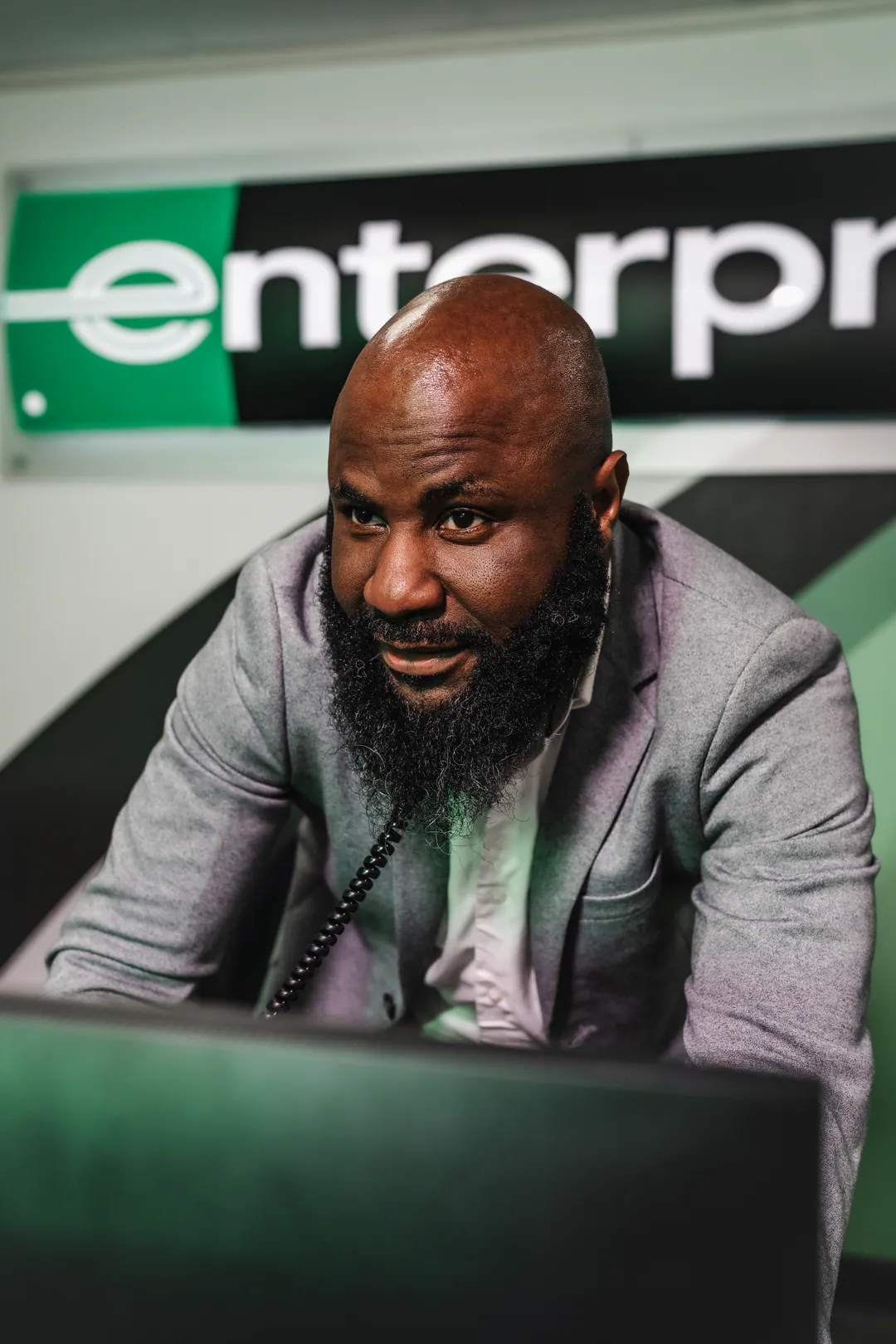 Bearded man in a grey blazer leaning over a computer screen beneath a green Enterprise sign