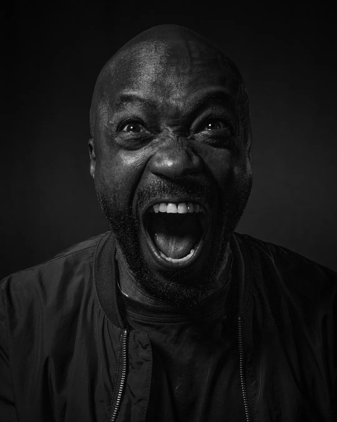 Bearded man in a bomber jacket shouting with his mouth wide open, black and white studio portrait