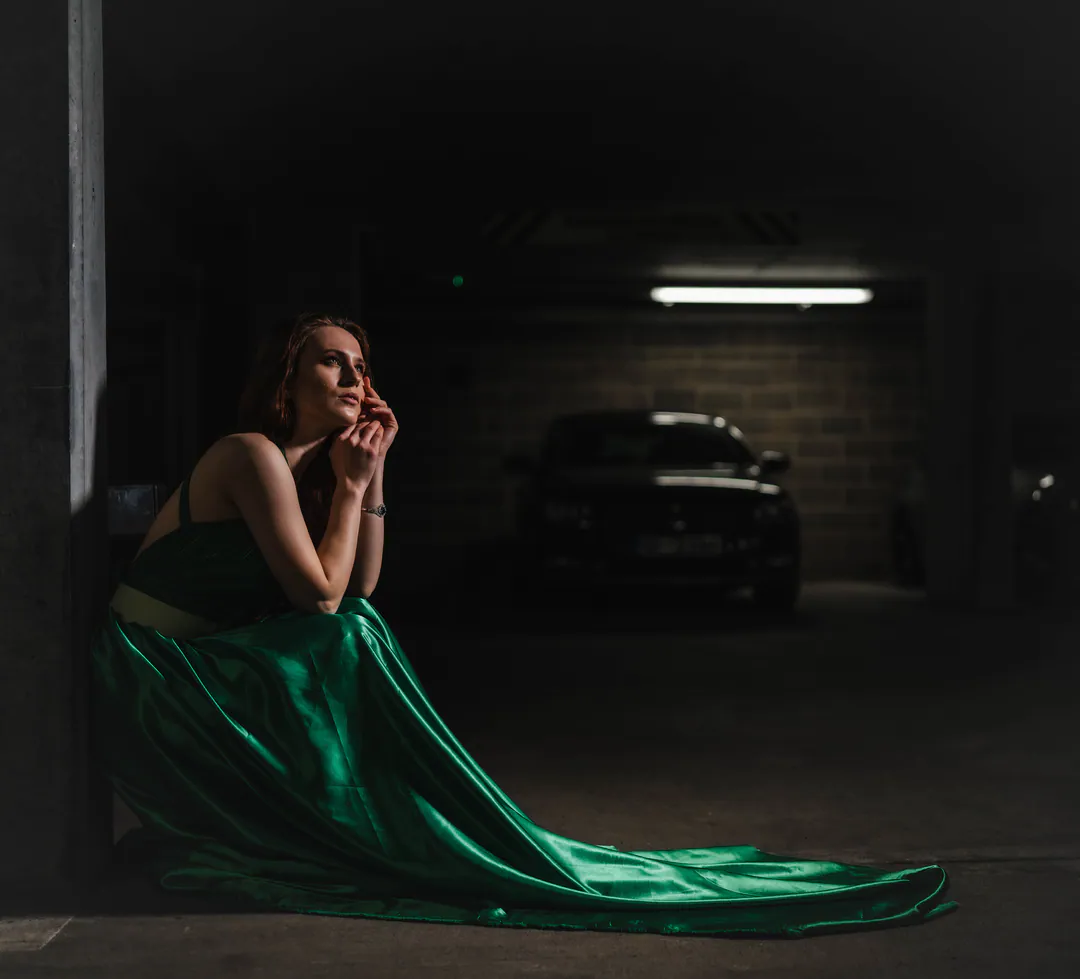 Woman in a green satin gown sitting on the floor of a dim underground car park