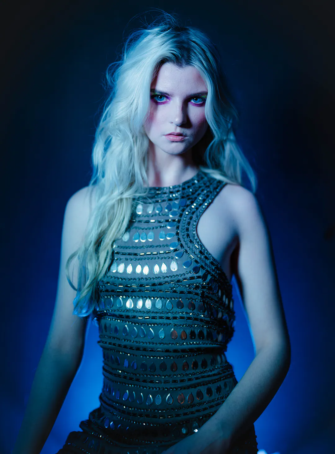 Woman with long platinum hair in an embellished sleeveless top, bathed in cool blue light